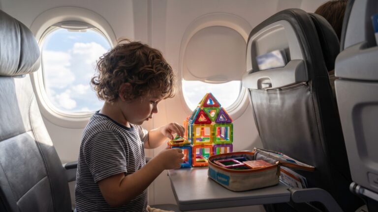 Young child building with colorful magnetic tiles on an airplane tray table during a flight